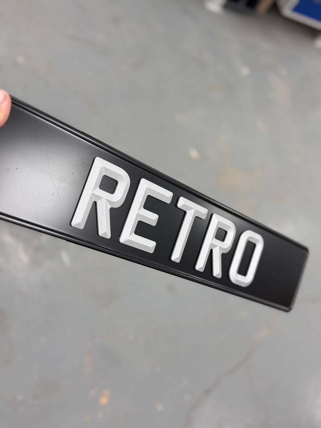 Black sign with 'RETRO' in white letters held by a hand on a gray floor.
