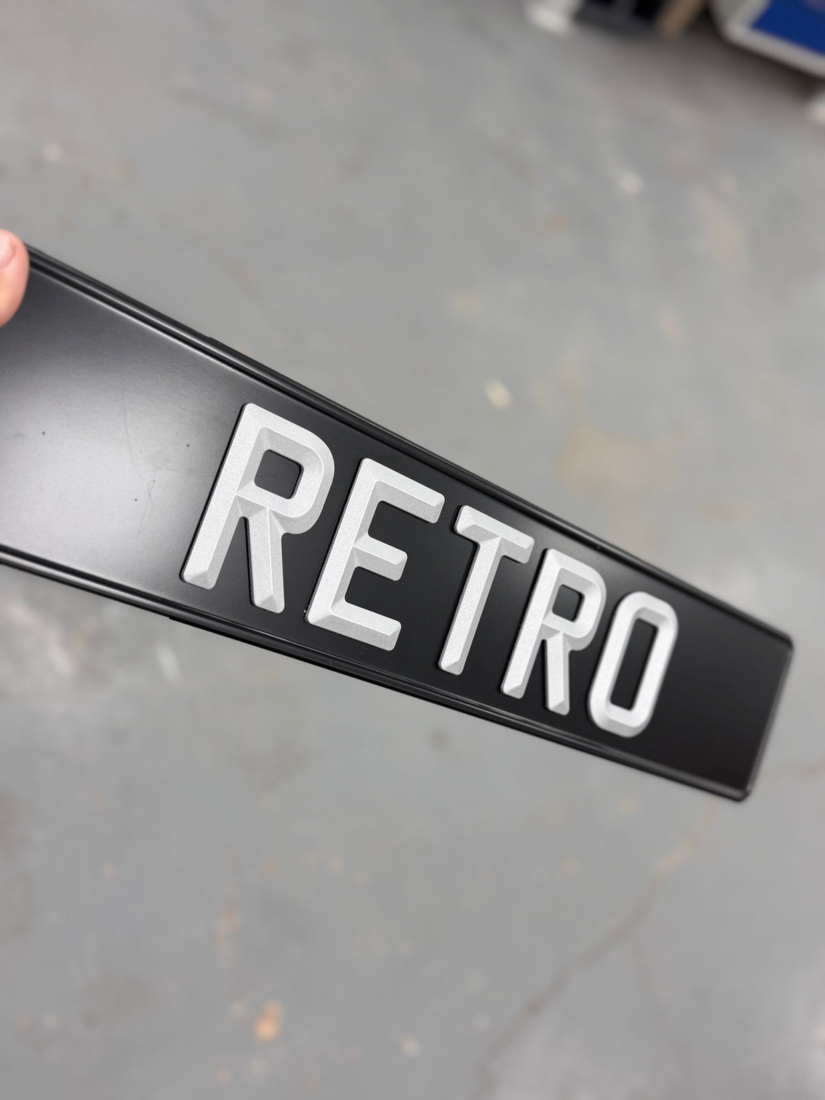 Black sign with 'RETRO' in white letters held by a hand on a gray floor.